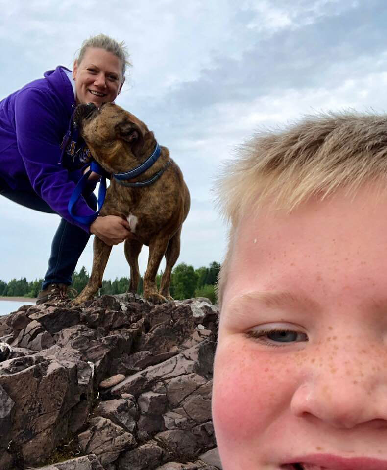 Candice hugging her bulldog on a lakeside cliff while Ayden takes a selfie