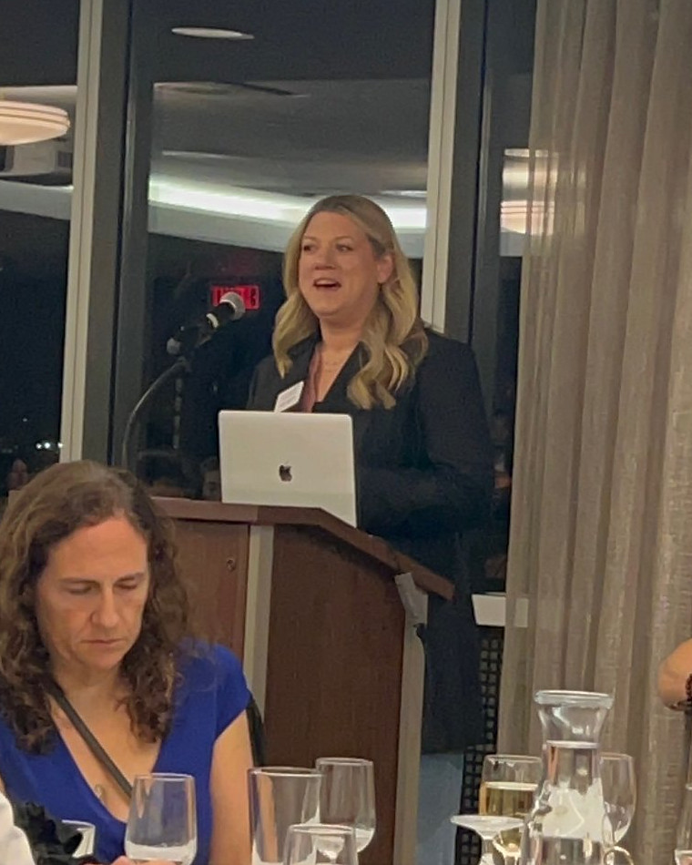 Candice Amundson speaking at a podium to a seated audience